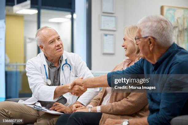 doctor greeting senior couple at hospital - couple shaking hands with doctor stock-fotos und bilder