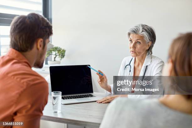 doctor discussing with couple in clinic - gp visit stock pictures, royalty-free photos & images