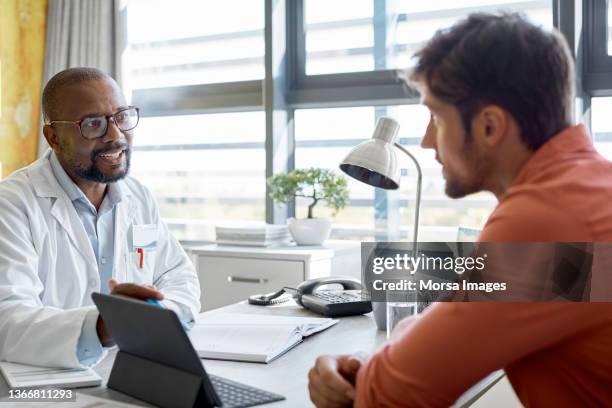 male doctor discussing with patient in clinic - varón fotografías e imágenes de stock