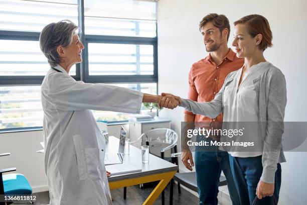 couple visiting female doctor in clinic - couple shaking hands with doctor stock pictures, royalty-free photos & images