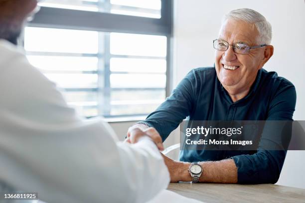 smiling man handshaking with doctor in clinic - arbeiten pflege senior stock-fotos und bilder