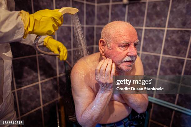 kaukasischer älterer männlicher patient, der sein gesicht während des assistierten bades wäscht - nurse with old male patient home care stock-fotos und bilder