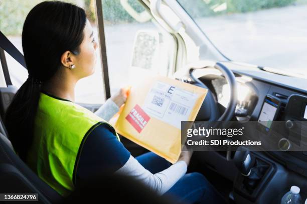 delivery woman driving while looking for address on envelope - delivery truck stock pictures, royalty-free photos & images