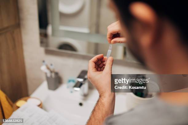 man drops swab in a protective plastic tube after nasal swab test to check for virus at home. - cotton swab stock pictures, royalty-free photos & images