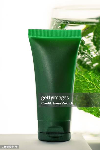close-up green tube with  moisturizing face cream or hand cream, shampoo, hair gel and  mint leaves in sparkling water with bubbles. - creme tube ストックフォトと画像
