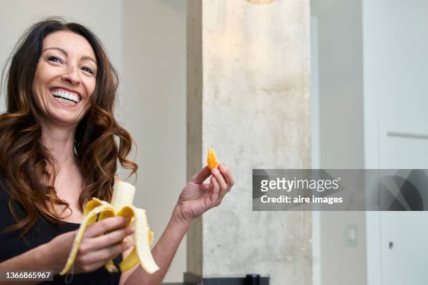 front view of woman looking to the side with a big smile while eating fresh fruits. - banane essen stock-fotos und bilder