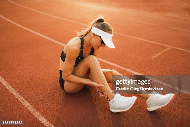 woman sitting on sports track and holding injured calf muscle. sprain ligament on running - female muscular calves stockfoto's en -beelden