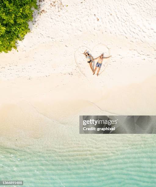 couple lying down on heart shape draw at beach - valentines day holiday stock pictures, royalty-free photos & images