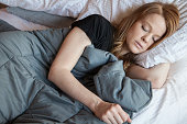 Young redhead woman using soft weighted blanket in her modern apartment
