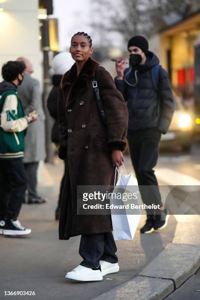 Model wears a black pullover, a brown suede with fur interior oversized long coat, black denim flared jeans pants, white leather sneakers from...