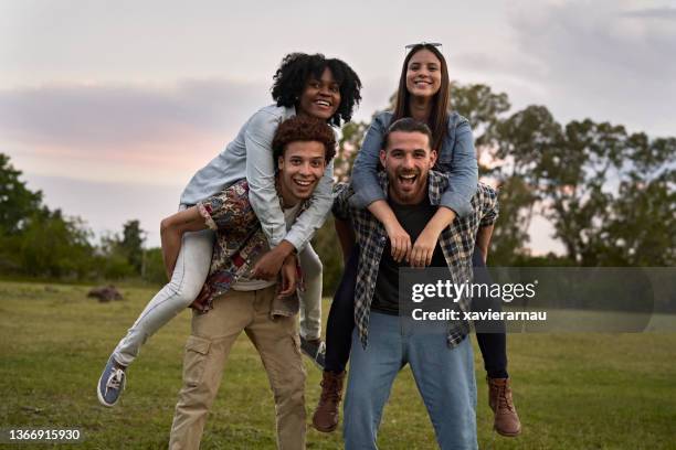 piggyback portrait of playful young friends outdoors at dusk - piggyback stock pictures, royalty-free photos & images
