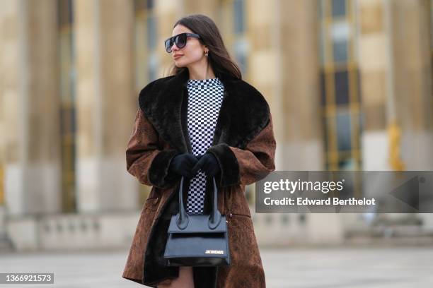 Bengi Guzel wears black futurist sunglasses, silver earrings, a black and white checkered print pattern high collar tube short dress, a brown suede...