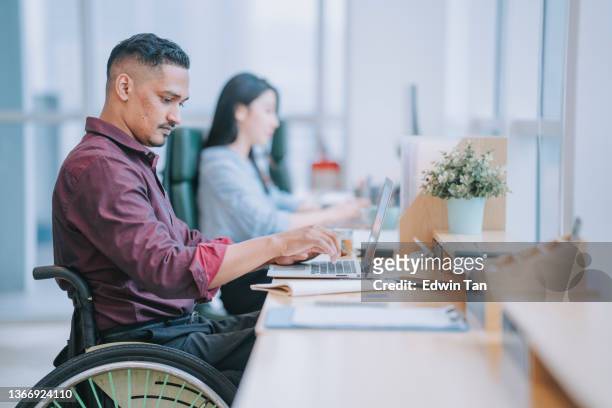 asian indian white collar male worker in wheelchair concentrating working in office beside his colleague - disability stock pictures, royalty-free photos & images