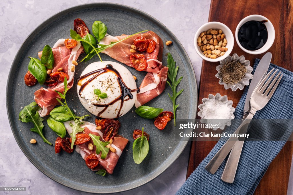 Queijo Burrata com presunto de parma e folhas de salada.
