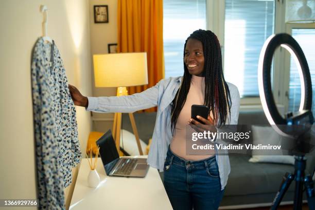 joven afroamericana tomando foto de una blusa usando su teléfono inteligente para vender o donar su ropa. - red blouse fotografías e imágenes de stock