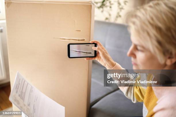 checking an invoice while taking a photo of a damaged delivery cardboard box - damaged box stock pictures, royalty-free photos & images