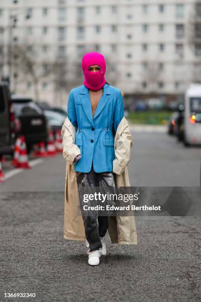 Guest wears a neon pink wool baclava, a silver double chains necklace, a blue nailed / studded blazer jacket, a beige long trench coat, black and...