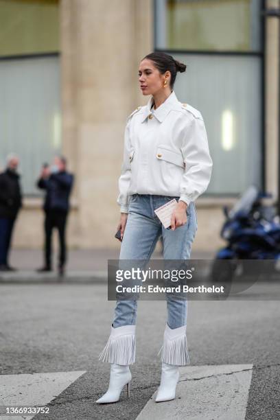 Guest wears black sunglasses, gold earrings, a white t-shirt, a white matte leather jacket, blue faded denim skinny jeans pants, white matte leather...