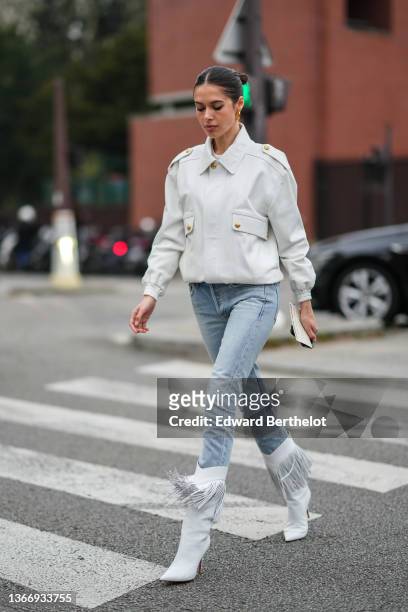 Guest wears black sunglasses, gold earrings, a white t-shirt, a white matte leather jacket, blue faded denim skinny jeans pants, white matte leather...