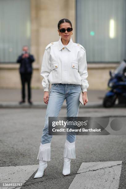 Guest wears black sunglasses, gold earrings, a white t-shirt, a white matte leather jacket, blue faded denim skinny jeans pants, white matte leather...