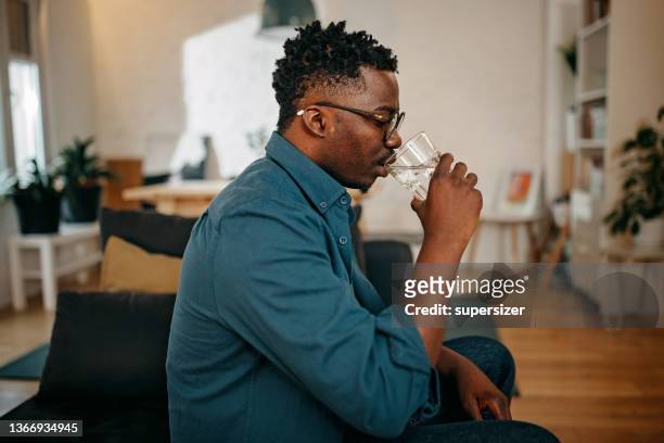 un jeune homme noir boit un verre d’eau - man drinking water photos et images de collection