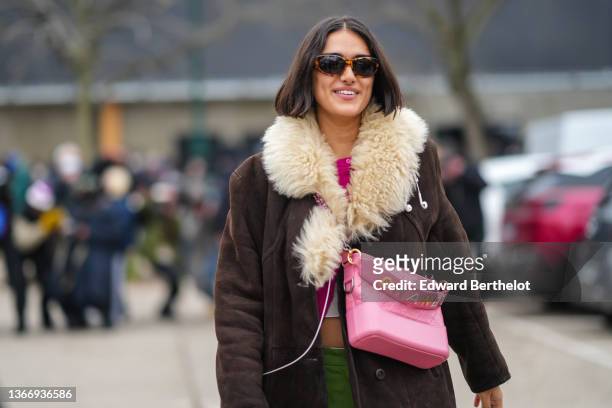 Model wears sunglasses, a neon pink pullover, a pale gray cropped t-shirt, a brown suede with pale yellow large sheep collar long coat, a pale pink...