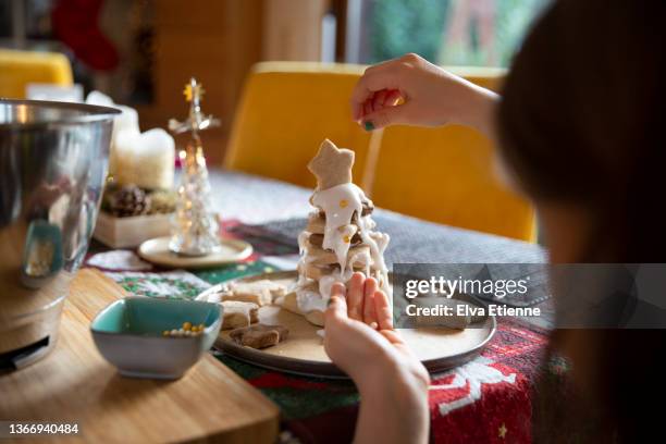 over the shoulder view of a child decorating a tower of star shaped, homemade christmas biscuits, with icing and edible sugar pearls, at a dining table. - girls hands behind back stock-fotos und bilder