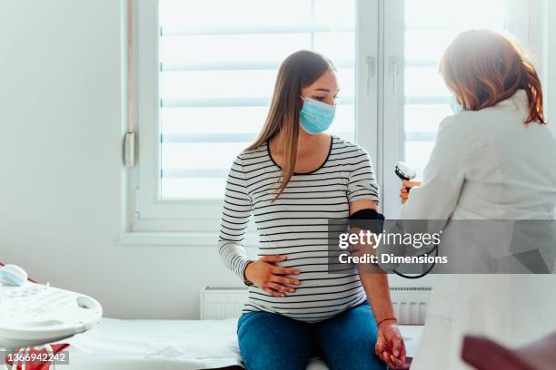 arzt mit einer schwangeren frau, die während einer untersuchung medizinische masken trägt - pregnant woman at doctor stock-fotos und bilder