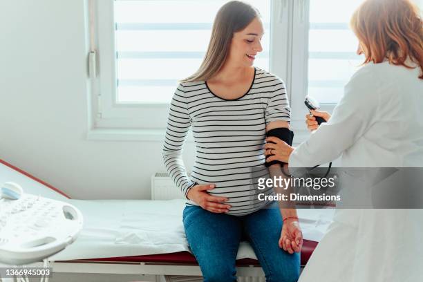 jeune femme enceinte vérifiant la tension artérielle au cabinet médical - blood pressure photos et images de collection