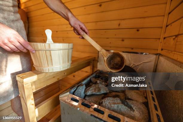 a man pouring water on hot stones in finnish sauna - sauna stock pictures, royalty-free photos & images