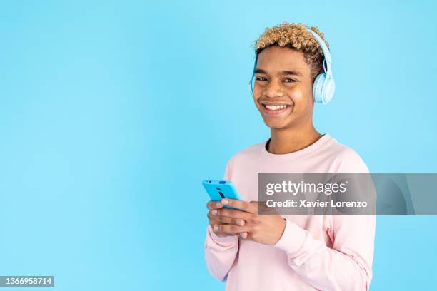 teenage boy using a mobile phone and headphones while standing o - boy portrait studio stock pictures, royalty-free photos & images