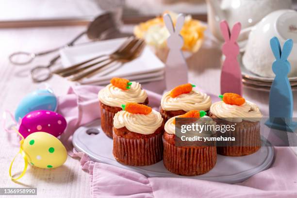carrot cake muffins with cream cheese, topped with marzipan carrots on a plate. delicious homemade dessert. - paastaart stockfoto's en -beelden