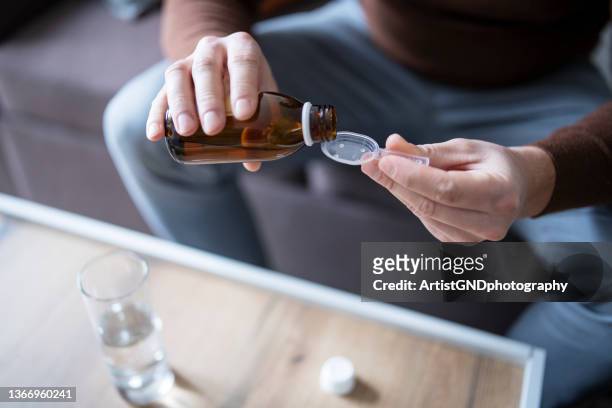 man pouring cough syrup into spoon. - syrup stockfoto's en -beelden
