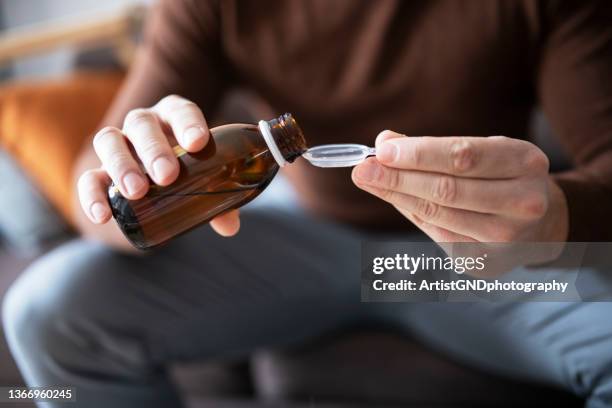 man pouring cough syrup into spoon. - cough medicine stock pictures, royalty-free photos & images