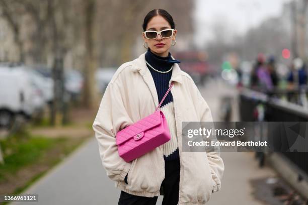 Guest wears white sunglasses, gold large earrings, a navy blue and white print pattern pleated / accordion turtleneck wool pullover, a white latte...