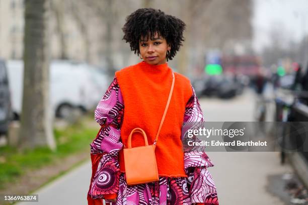 Guest wears gold earrings, a neon orange felt / fluffy sleeveless pullover, a pink / white / orange / black print pattern puffy / ruffled oversized...