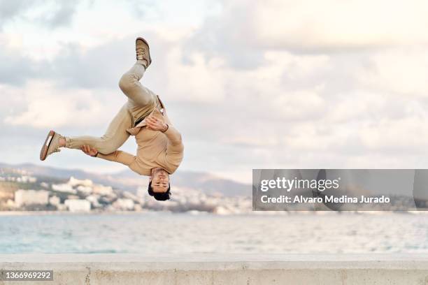 man doing somersault above ground on seafront - somersault stock pictures, royalty-free photos & images