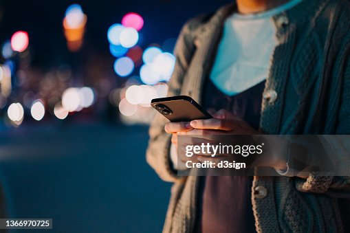 Close up, mid-section of young Asian woman using smartphone in illuminated and multi-coloured city at night. Lifestyle and technology Close up, mid-section of young Asian woman using smartphone in illuminated and multi-coloured city at night. Lifestyle and technology