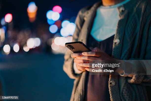 close up, mid-section of young asian woman using smartphone in illuminated and multi-coloured city at night. lifestyle and technology - telegram stock pictures, royalty-free photos & images