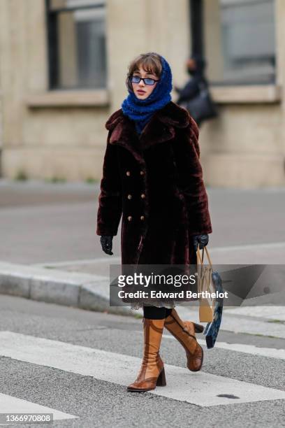 Guest wears a blue fluffy baclava / scarf, black sunglasses, a brown fluffy long coat, black tights, black shiny leather gloves, a blue / green /...