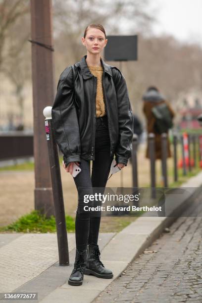 Model wears a brown and gold fluffy wool, a black shiny leather oversized jacket, a black shiny leather back pack bag, black skinny denim jeans...