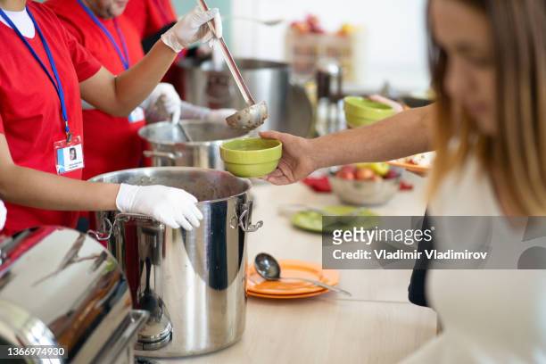 una línea de manos sirviendo comida en un comedor de beneficencia - stew pot fotografías e imágenes de stock