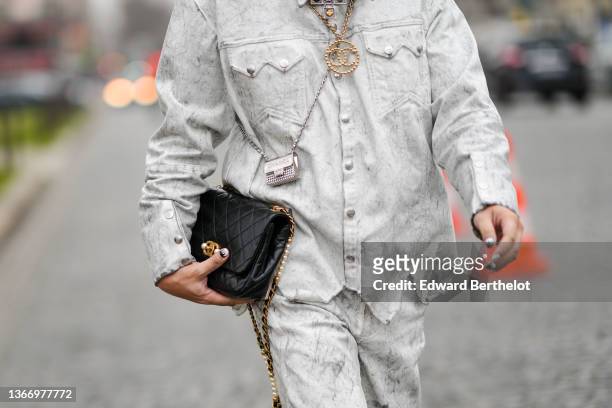 Declan Chan wears pale gray faded denim jacket, matching pale gray faded large denim jeans pants, a black shiny leather Timeless handbag from Chanel,...