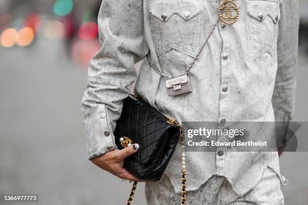 Declan Chan wears pale gray faded denim jacket, matching pale gray faded large denim jeans pants, a black shiny leather Timeless handbag from Chanel,...