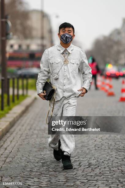 Declan Chan wears pale gray faded denim jacket, matching pale gray faded large denim jeans pants, a black shiny leather Timeless handbag from Chanel,...