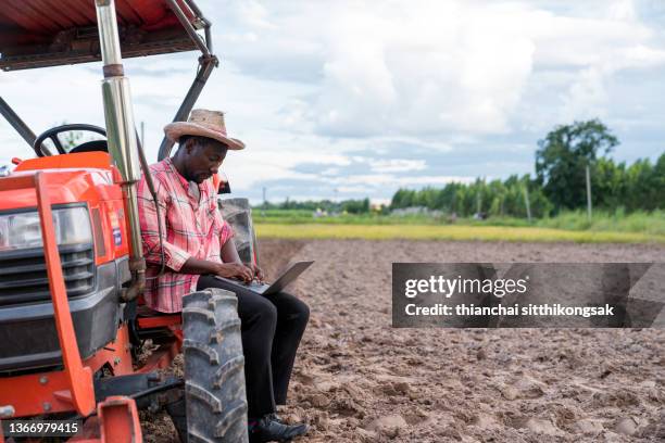 shot of young farmer using laptop,counts yields in field. - african american farmer stockfoto's en -beelden