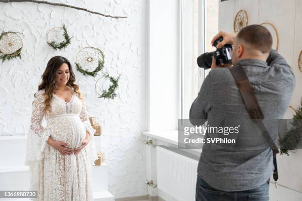 der professionelle fotograf fotografiert ein schwangeres model im studio. - umstandskleidung stock-fotos und bilder