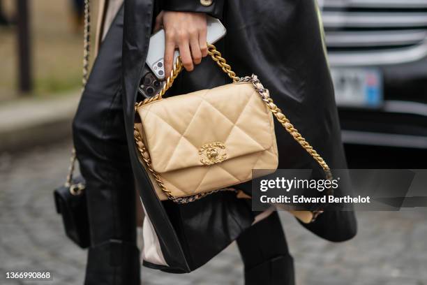 Guest wears a half black and half beige shiny leather long trench coat, black shiny leather large pants, a beige shiny leather Chanel 19 handbag form...