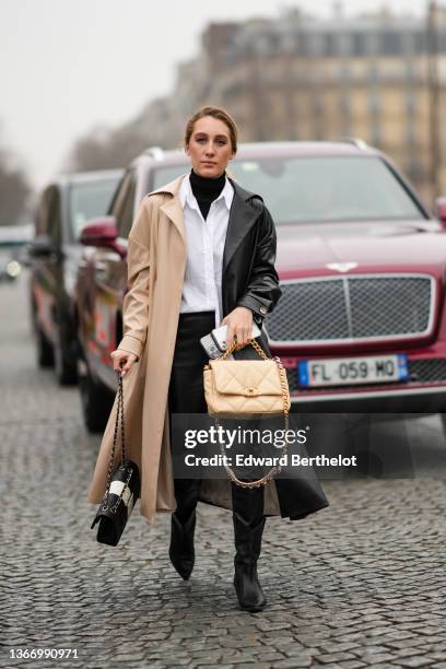 Guest wears a black turtleneck pullover, a white shirt, a half black and half beige shiny leather long trench coat, black shiny leather large pants,...