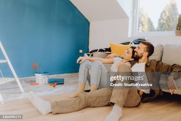 young couple paint together a wall in their apartment - couple working from home stock pictures, royalty-free photos & images